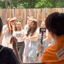 a group of young women are dancing in front of a wooden fence while a man takes a picture of them .