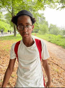 a young boy wearing glasses and a hat is standing on a path in a park