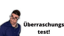 a man wearing glasses and a blue shirt is standing next to a sign that says überraschungs test .