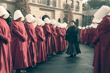 a man in a black hat stands in front of a group of nuns in red robes