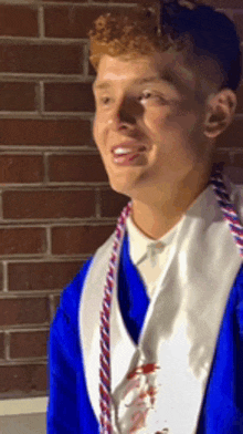 a young man wearing a blue and white graduation cap and gown is smiling in front of a brick wall .