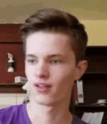 a young man in a purple shirt is looking at the camera .