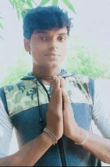 a young man wearing a camouflage vest is holding his hands together in prayer