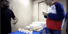 a man wearing a red white and blue jacket with the word helmet on it stands in front of a table full of food