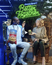 snoop dogg sitting next to a woman holding a bag of tostitos chips