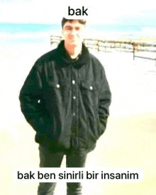 a man in a black jacket is standing in front of a beach .