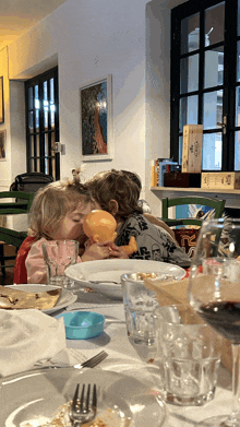 two little girls are sitting at a table playing with a doll that says ' coca cola ' on the front