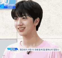 a young man wearing a pink shirt is smiling in front of a sign that has chinese writing on it