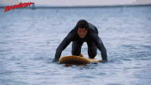 a man in a wetsuit is kneeling on a surfboard in the water with the word baywatch written in red