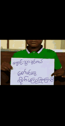 a man in a green shirt is holding up a sign in a foreign language .