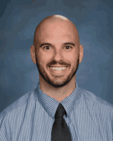 a man with a beard wearing a blue shirt and tie smiles for the camera