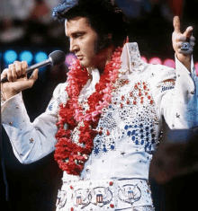 a man with a lei around his neck is singing into a microphone with his hands in the air