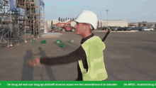 a man wearing a hard hat and a green vest is standing in a parking lot with bottles on the ground