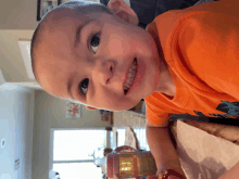 a young boy in an orange shirt looks at the camera and smiles