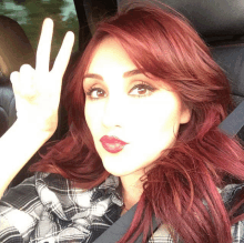 a woman with red hair is wearing a plaid shirt and giving a peace sign