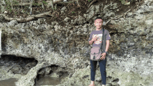 a man standing in front of a rock wall with a pink purse