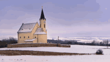 a small yellow church with a black steeple and a cross on top