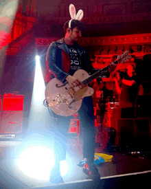 a man wearing bunny ears plays a guitar on stage