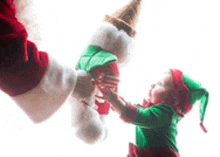 a little girl dressed as an elf is reaching for a christmas ball .