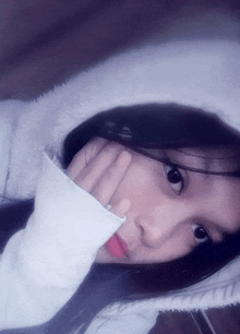 a girl wearing a white hoodie is taking a selfie with her hand on her face