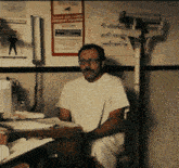 a man in a hospital gown sits at a desk in front of a sign that says ' ambulance '