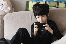 a young boy is sitting on a couch playing a game on a cell phone