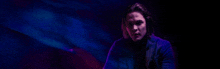 a man with long hair is standing in a dark room with a blue light behind him .