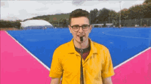 a man wearing glasses and a yellow shirt is standing in front of a pink and blue tennis court