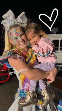 a little girl is being held by a woman with itsjojosiwa written on the bottom of the photo