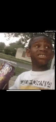 a young boy in a california shirt is holding a purple soda can .