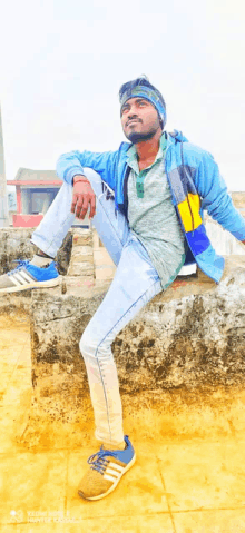 a man sitting on a brick wall with his legs crossed wearing a blue jacket and adidas shoes