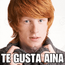 a young man with red hair is wearing a grey sweater and has the words te gusta aina on his face