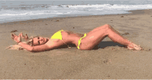 a woman in a yellow bikini is laying in the sand on the beach .