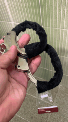 a hand is holding a pair of handcuffs with a black furry cuff