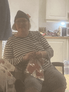 a woman wearing a black hat and striped shirt is knitting in a kitchen