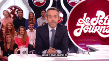 a man in a suit and tie is sitting at a table in front of a sign that says le petit journal