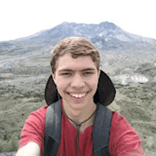 a young man in a red shirt is taking a selfie with a backpack .