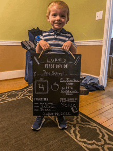 a young boy is holding up a chalkboard that says luke 's first day of preschool