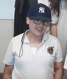 a boy wearing a ny hat and glasses smiles