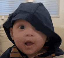 a baby is wearing a blue hooded hat and making a funny face .