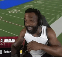 a man wearing headphones and a white tank top is sitting in front of a football field with the word alabama on it