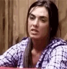 a woman in a plaid shirt is sitting at a table with a wooden wall in the background .