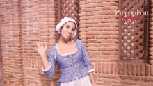 a woman in a blue dress stands in front of a brick wall and a sign that says puy du fou espana