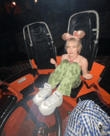 a girl with a pink bow on her head sits in an orange chair