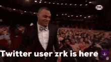 a man in a suit stands in front of a crowd with the words twitter user zrk is here