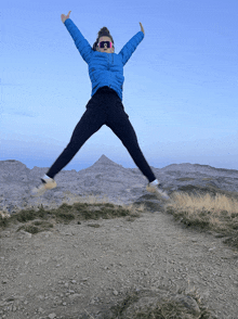 a woman in a blue jacket is jumping in the air with her arms outstretched