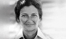 a black and white photo of a woman in a white shirt and tie smiling .