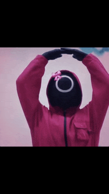 a person wearing a red jacket and a black mask with a pink bow on it .