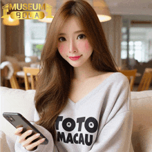 a woman wearing a shirt that says toto macau holding a cell phone