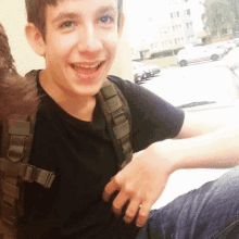 a young boy wearing a black shirt and a backpack smiles for the camera .